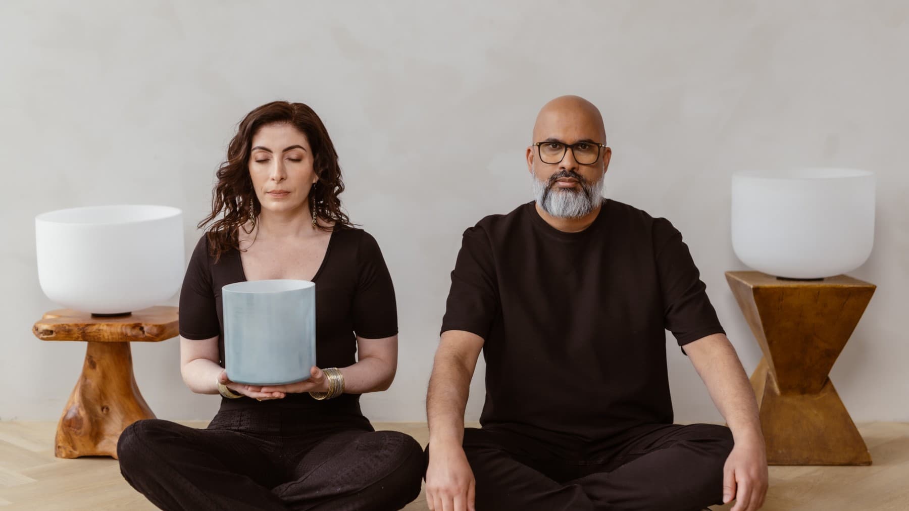 Jennifer holding a crystal bowl with her eyes closed, seated on the floor beside Steve, with two large crystal bowls on wooden stands behind them
